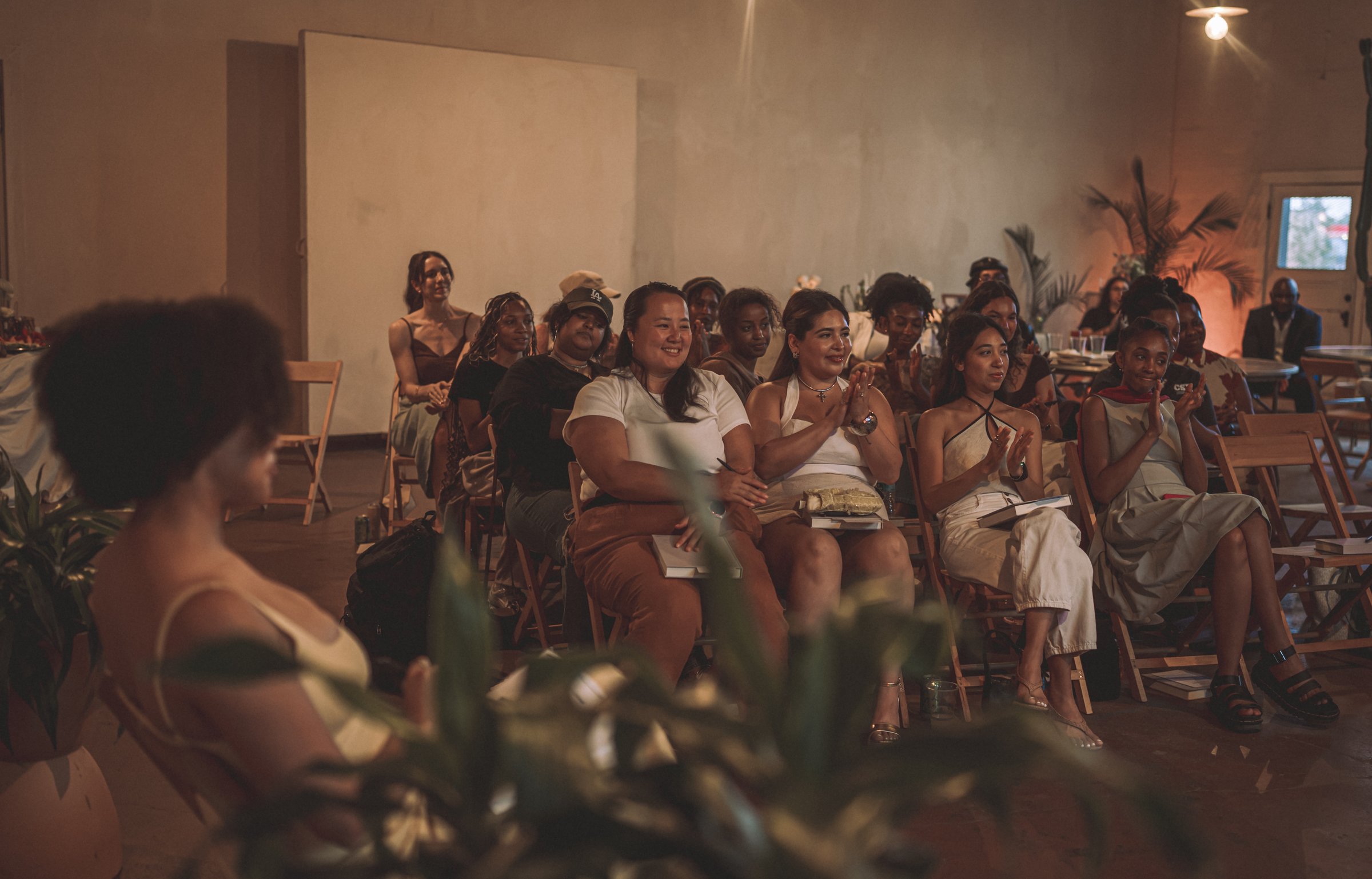 Rows of women seated in folding chairs in a sunlit room at Mother Plant Co., listening together at the founding gathering.